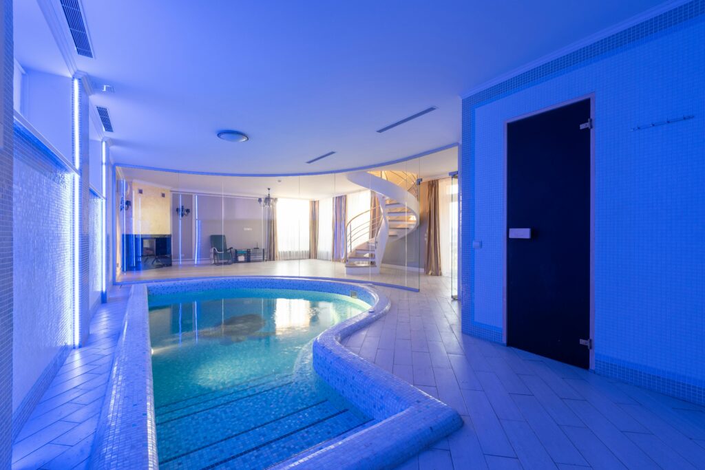 Swimming pool with clear water placed in spacious room at wall with blue illumination and staircase in contemporary luxury house